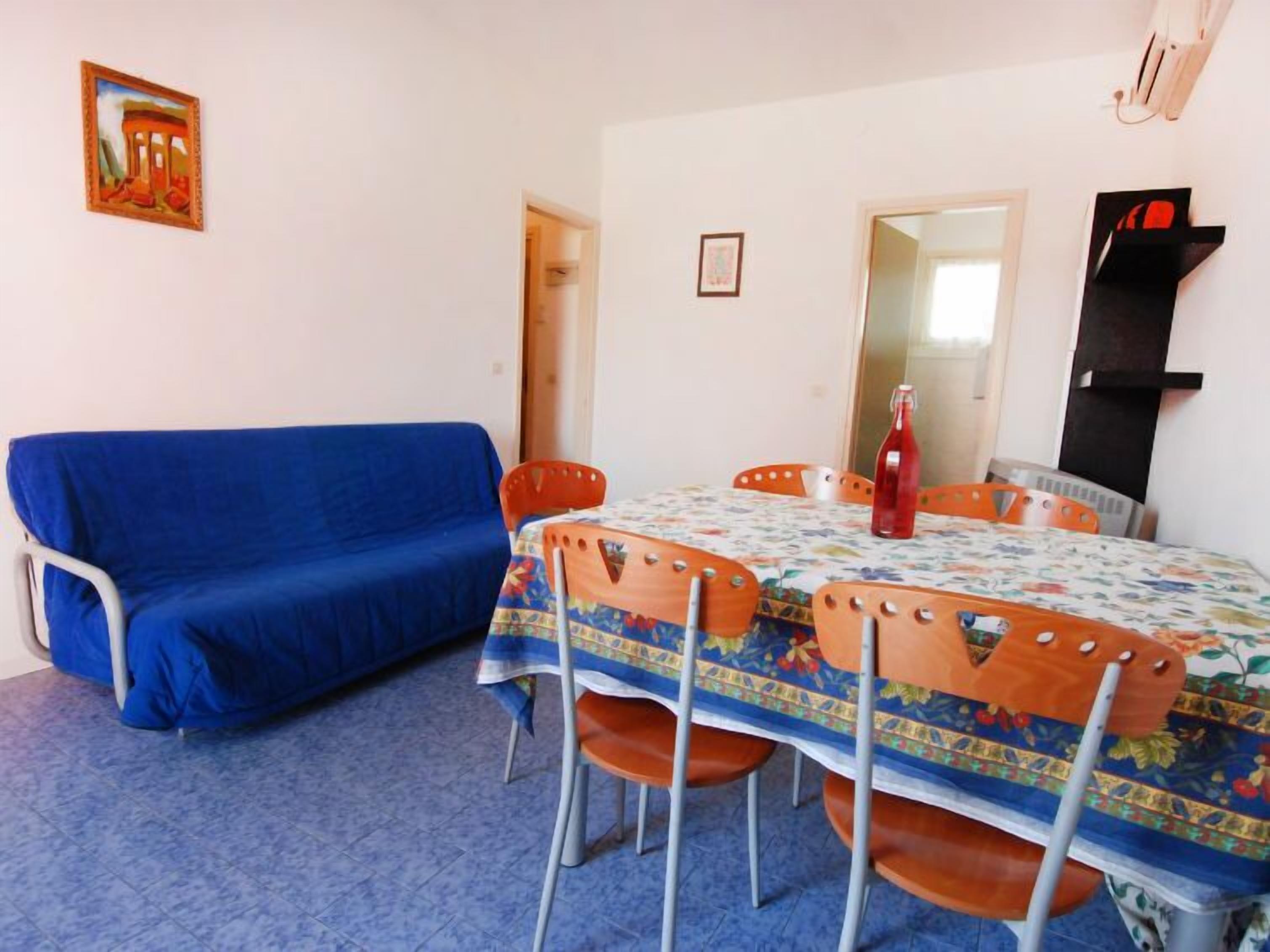 Una habitación con un sofá azul, una mesa con mantel floreado y sillas naranjas.