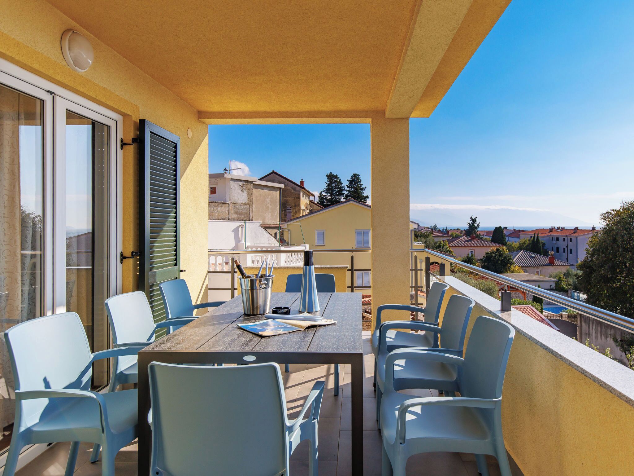 A balcony with a wooden table and chairs, a bottle of wine, and a menu.