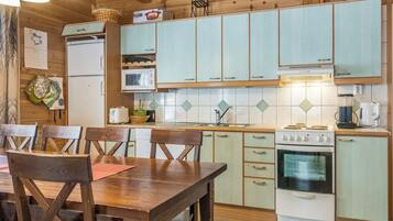 Een keuken met houten keukenkastjes, een fornuis, een magnetron en een eettafel met stoelen.