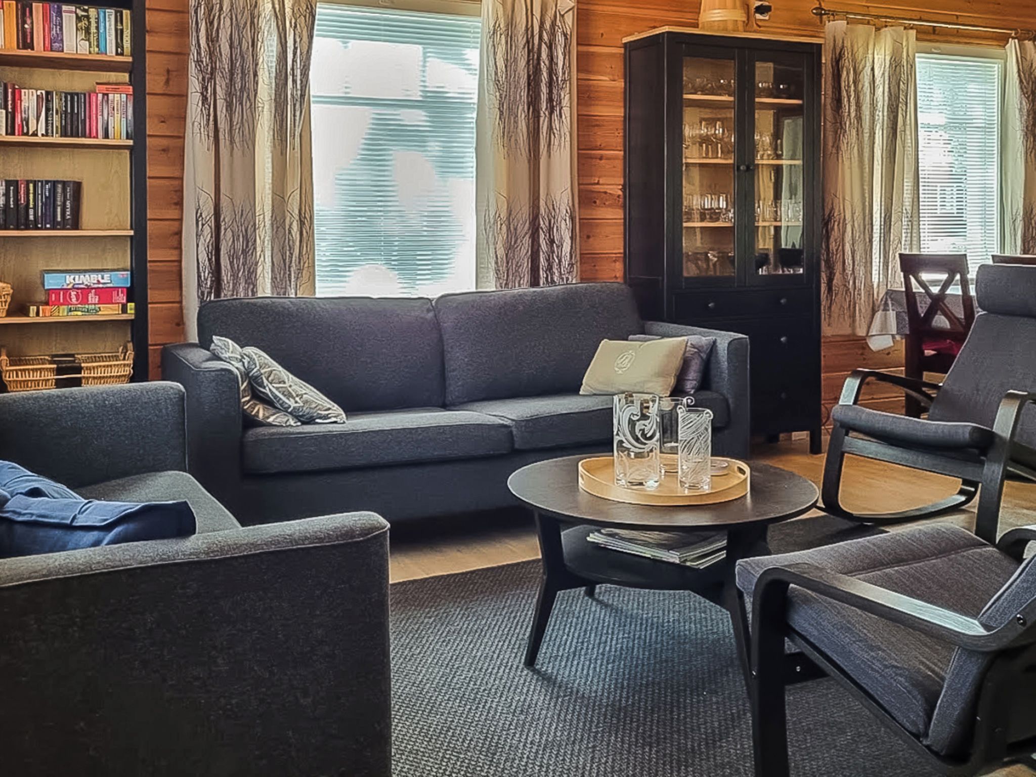 Een gezellige woonkamer met een bank, fauteuils, een bijzettafeltje en een boekenkast.
