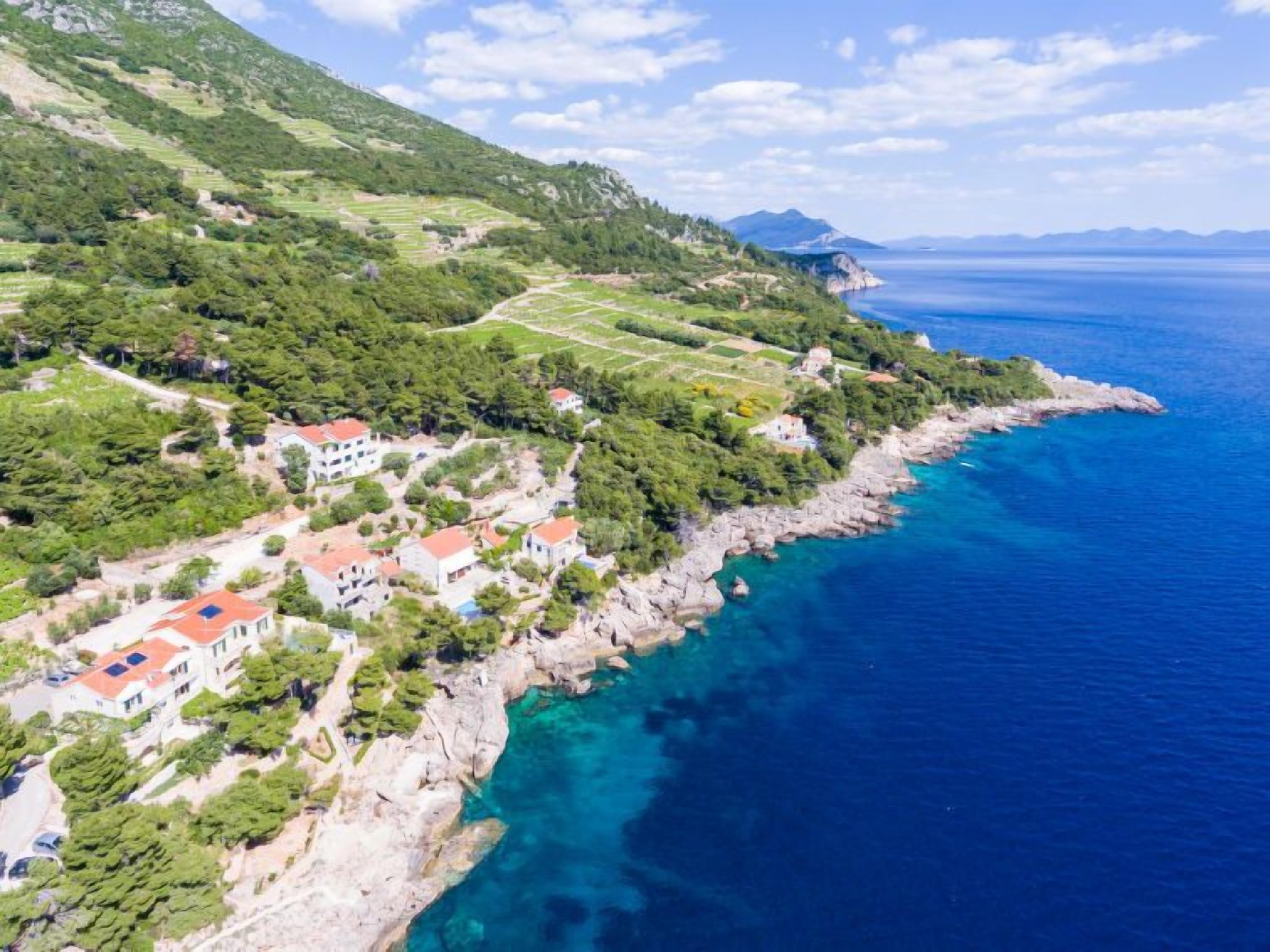 Un village côtier avec des champs en terrasses, des maisons aux toits rouges et une vue dégagée sur la mer.