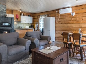 Interior acogedor de una cabaña con chimenea, sofá, mesa de comedor y zona de cocina.