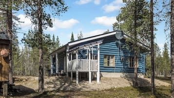 A log cabin with a porch, surrounded by trees.