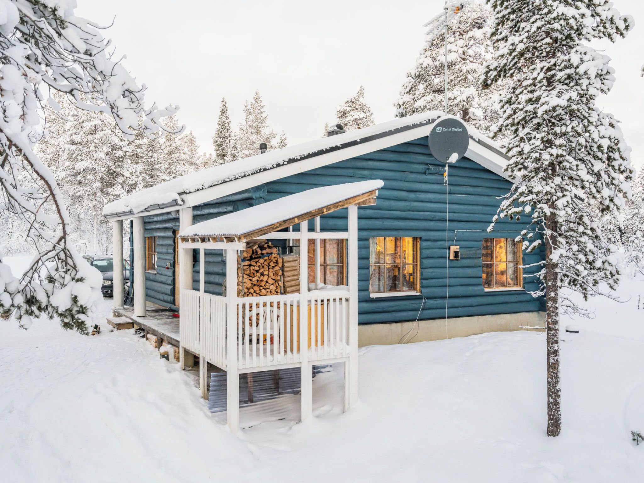 A log cabin with a porch, a satellite dish, and a stack of firewood.