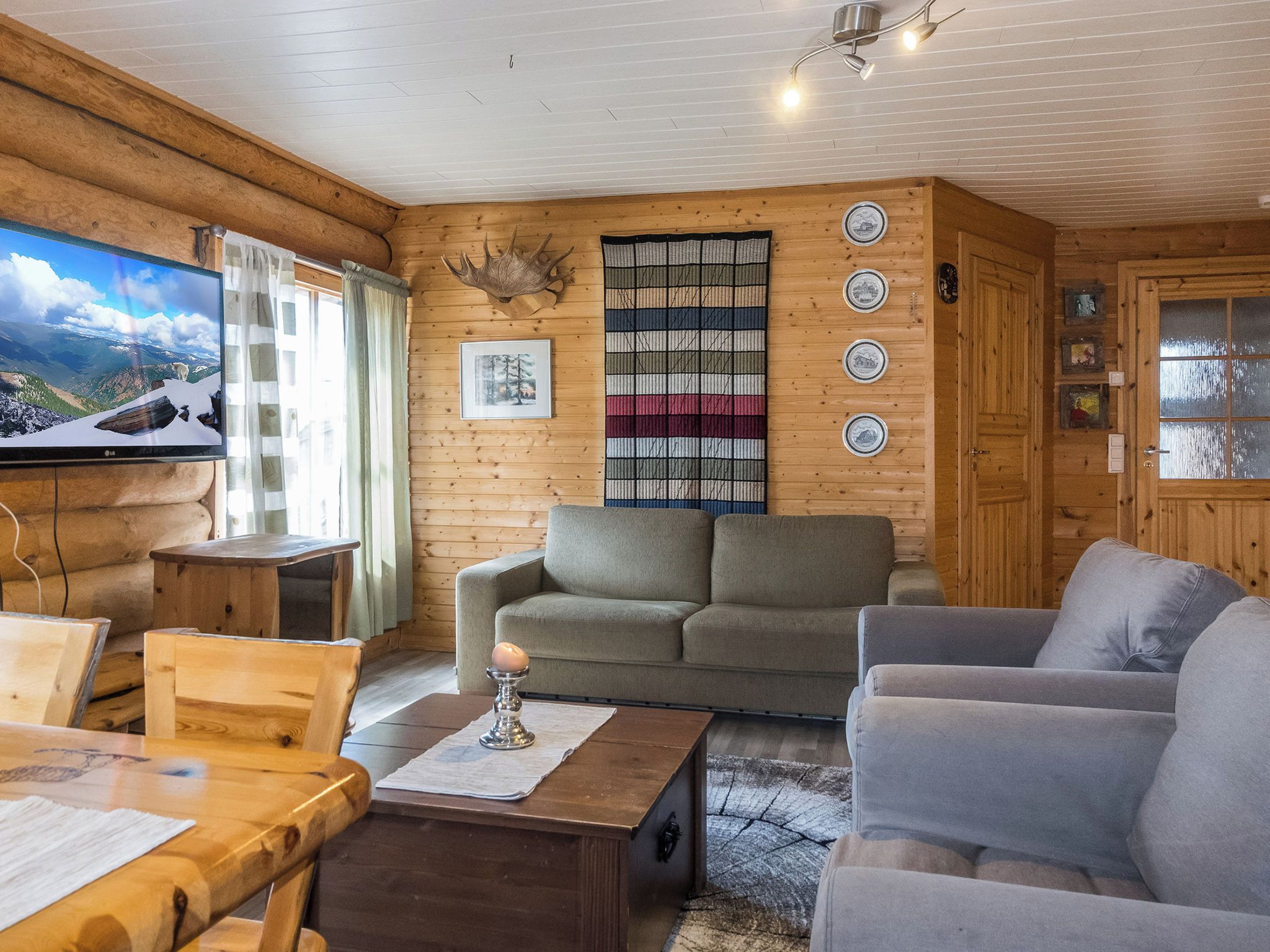 L’intérieur chaleureux d’un chalet en bois comprend une télévision, une cheminée et offre une vue sur un paysage montagneux enneigé.