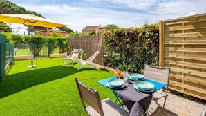 Une terrasse avec une table dressée pour le repas, entourée d’une pelouse bien entretenue et d’une clôture en bois.