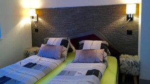 Una cama doble con colcha a rayas, dos almohadas y un cabecero con textura. A ambos lados de la cama hay dos lámparas fijadas a la pared.