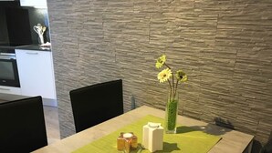 Un comedor con una mesa dispuesta para dos personas, un florero con flores amarillas y una cocina moderna al fondo.