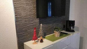 Una cocina moderna con protector mural de piedra, un televisor de pantalla plana sobre una encimera blanca y una cafetera en la encimera.