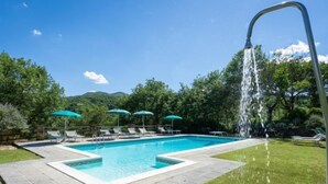 A rectangular swimming pool with a waterfall feature, surrounded by a paved deck and grass. - La Badia by Interhome (Vicchio)