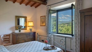 A bedroom with a bed, a dresser, a chair, a table with breakfast items, a window with a view, and a mirror. - La Badia by Interhome (Vicchio)