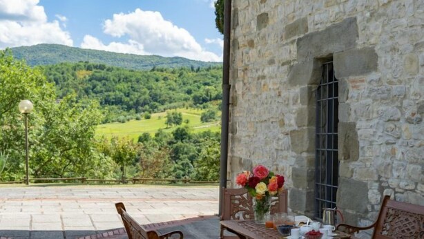 A stone building with a table and benches, a vase of flowers, and a view of green hills. - La Badia by Interhome (Vicchio)
