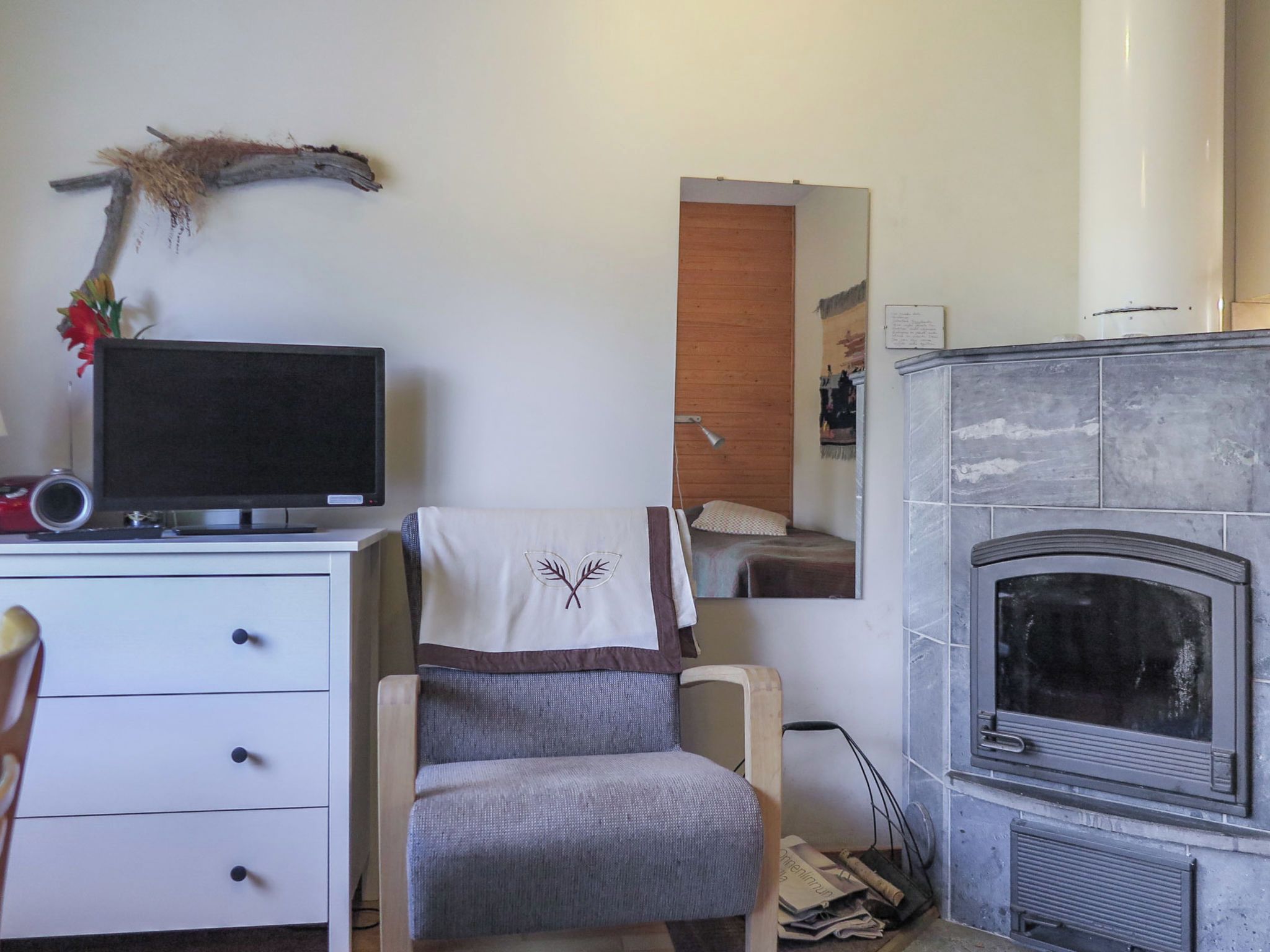 Een kamer met een televisie op een bureau, een open haard, een stoel en een spiegel aan de muur.