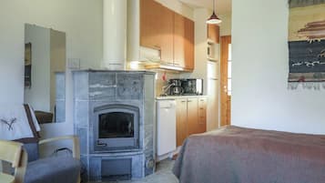 Een knus kamertje met een open haard, houten kasten, een kitchenette en een bed met een dekbed.
