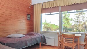 Quarto com duas camas, uma mesa de madeira e janela com vista para árvores.
