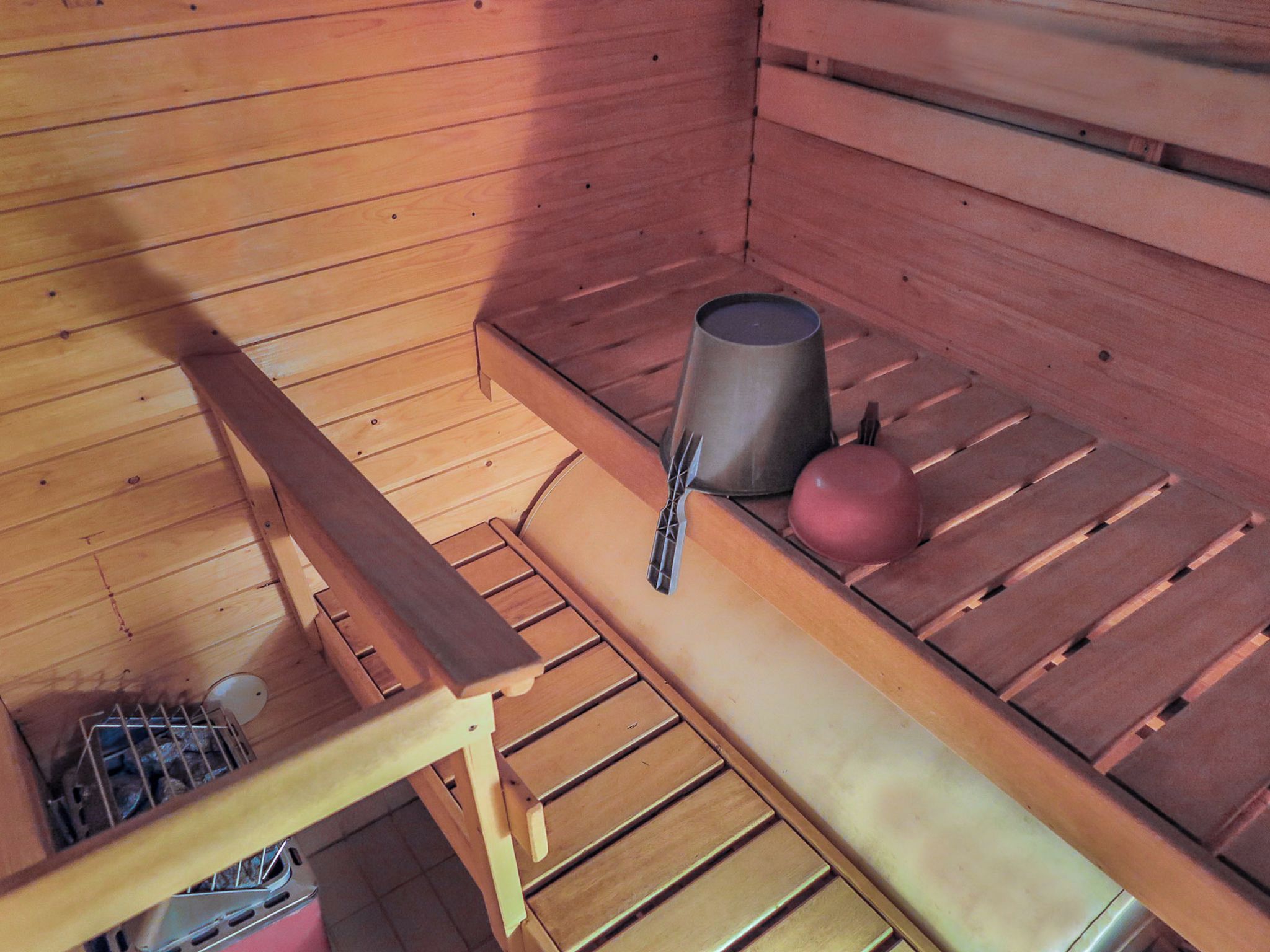 Een sauna met houten banken, een metalen emmer en een bolvormig object op een plank.