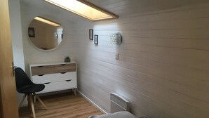 Un dormitorio con cama, escritorio y silla. Hay un espejo sobre el escritorio y un radiador en la pared.