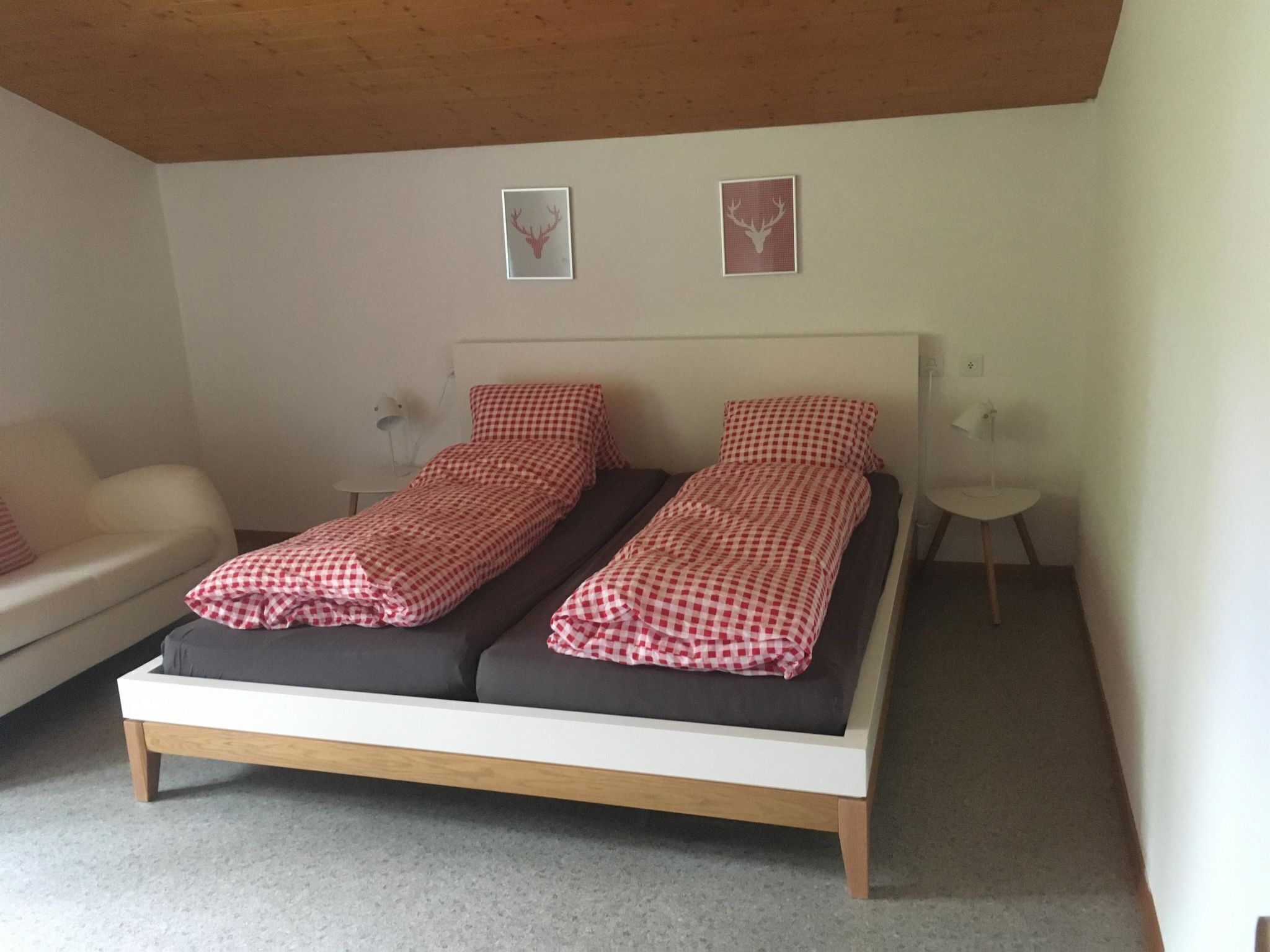 Ett sovrum med en säng, två sängbord, ett litet runt bord och två inramade tavlor på väggen.