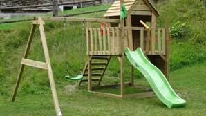 Una casita de juegos de madera con un tobogán y un columpio.