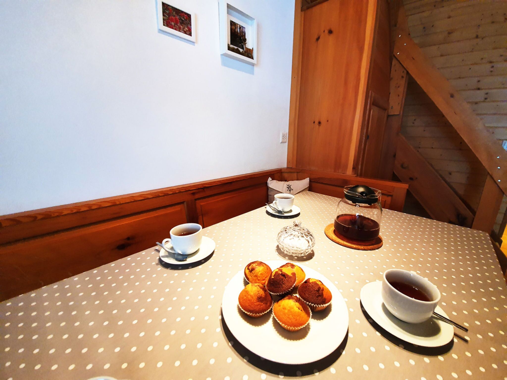 Une table à manger recouverte d’une nappe à pois, une théière, une tasse de thé, une assiette de muffins et une tasse de café.