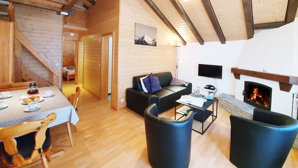 Acogedor interior de cabaña con comedor, sofá, chimenea y escalera.
