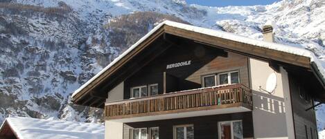 Ein mehrstöckiges Gebäude mit Balkon, mit der Aufschrift "BERGDÖHLE", vor einer verschneiten Berglandschaft.