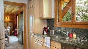 A kitchen with wooden cabinets, a granite countertop, a Siemens dishwasher, and a window with a view of trees. - Khamariah by Interhome (Villars)