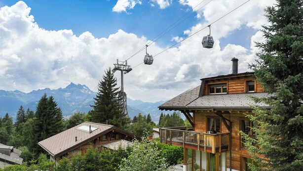 A wooden chalet with a balcony overlooking a mountainous landscape, a cable car system, and a well-maintained garden. - Khamariah by Interhome (Villars)