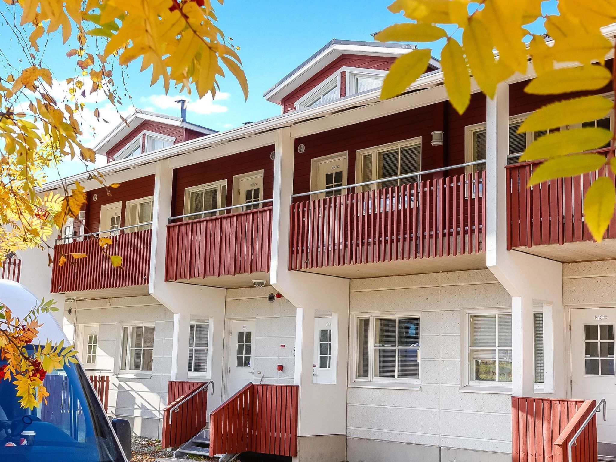 En række røde og hvide bygninger med altaner, en synlig dør og et lille vindue.