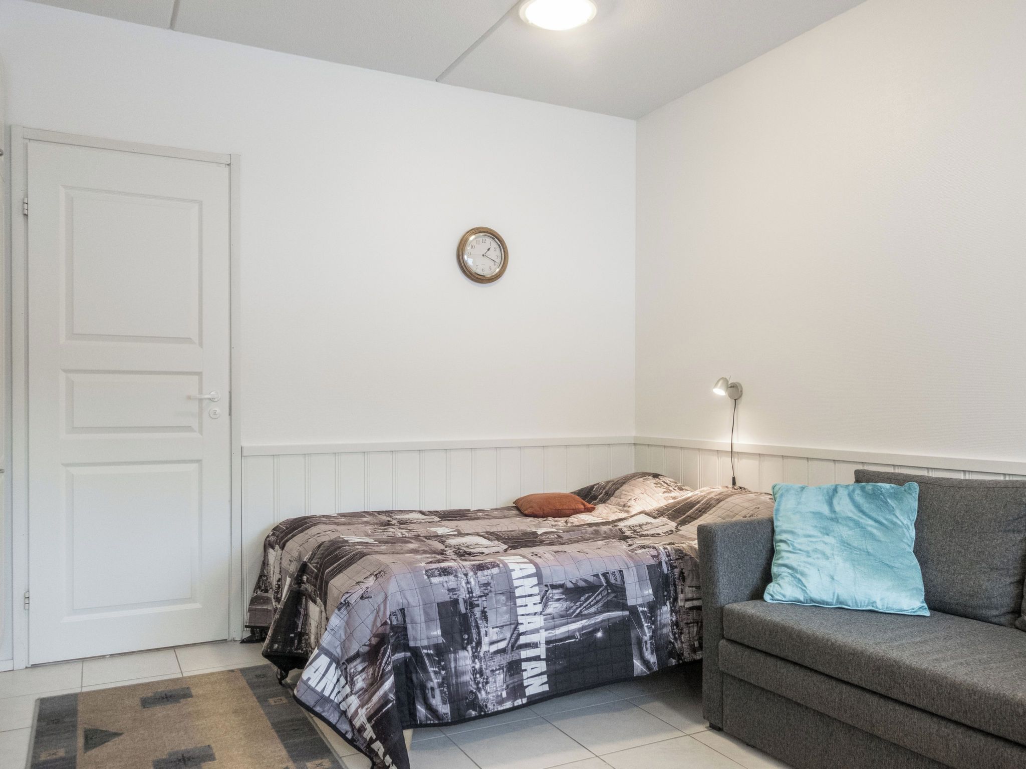 A bedroom with a bed, a sofa, a wall clock, and a door.