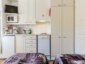 Cocina compacta equipada con microondas, tostadora, cafetera y lavavajillas. Cuenta con dos camas con ropa de cama estampada.