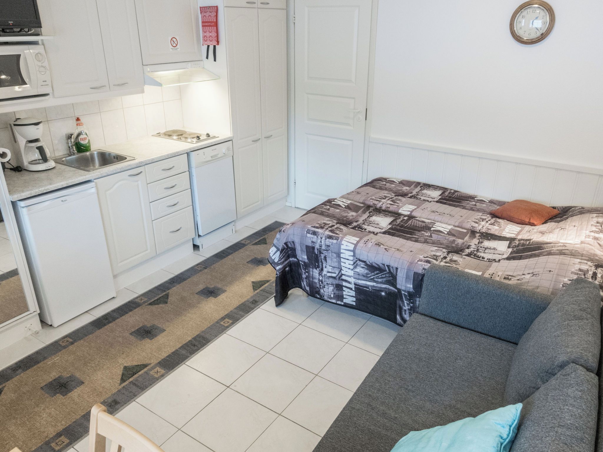 A compact living space with a kitchenette, a bed with a patterned bedspread, and a small seating area.