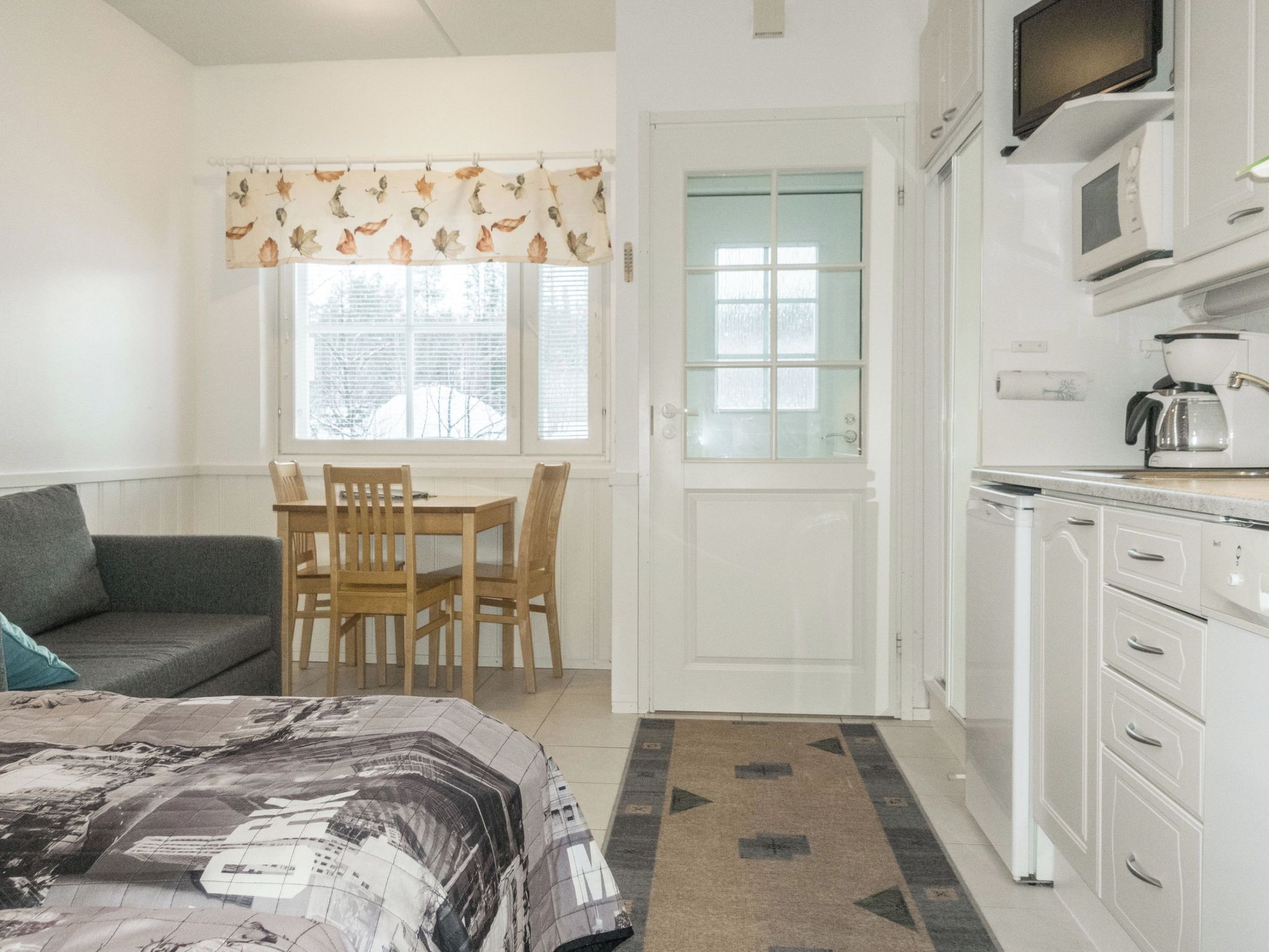 A compact room with a bed, a dining table with chairs, a kitchenette, and a door leading to another room.