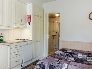 A compact room with a kitchenette, a shower, and a bed with a patterned bedspread.