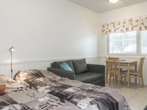 A bedroom with a bed, a grey sofa, a wooden table with chairs, a floor lamp, and a window with a leaf-patterned curtain. - Levi star 1503 by Interhome (Kittilä)