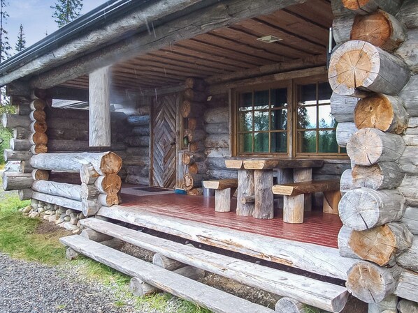 A log cabin with a porch, wooden benches, and a stone fireplace.