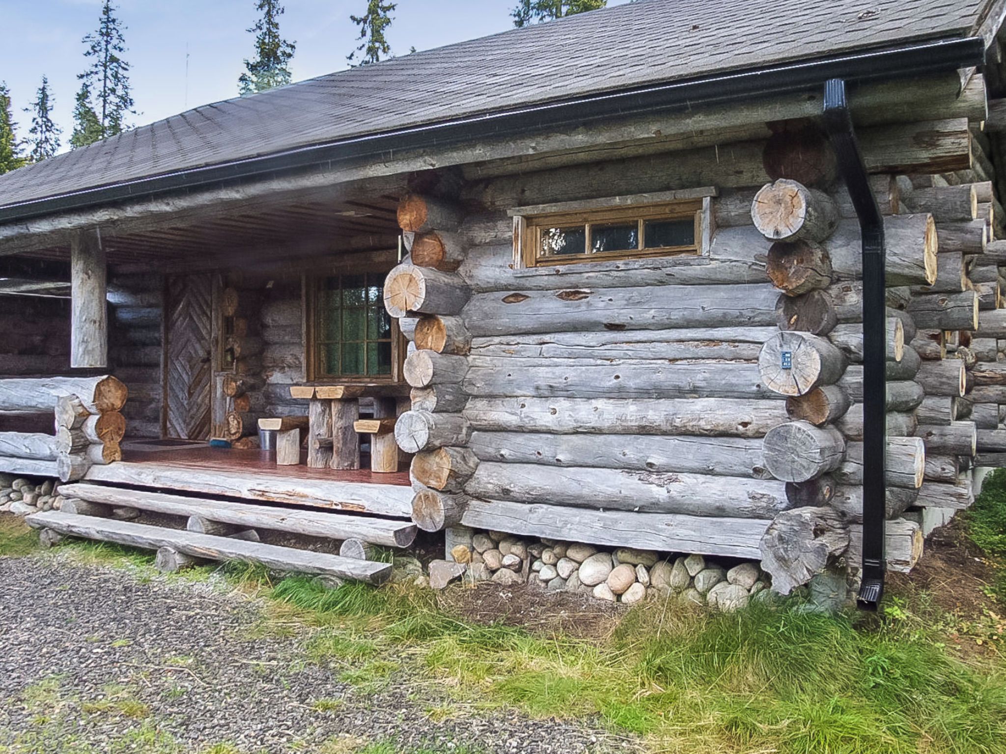 A log cabin with a porch, stone foundation, and a window.