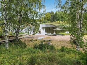 Un camping paisible au bord d’un lac, avec un quai, des tables de pique-nique et un bateau.