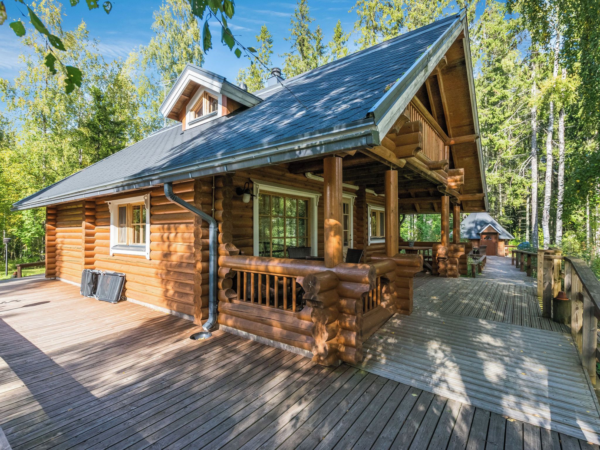 Eine Blockhütte mit Veranda und Terrasse, umgeben von Bäumen.