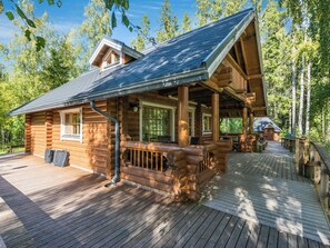 A log cabin with a porch and deck, surrounded by trees.