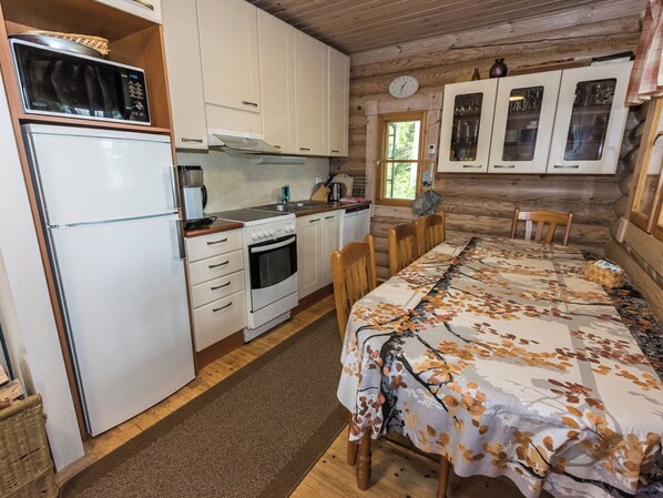 A compact kitchen with a refrigerator, stove, and sink, wooden cabinets, and a dining area with a table and chairs.