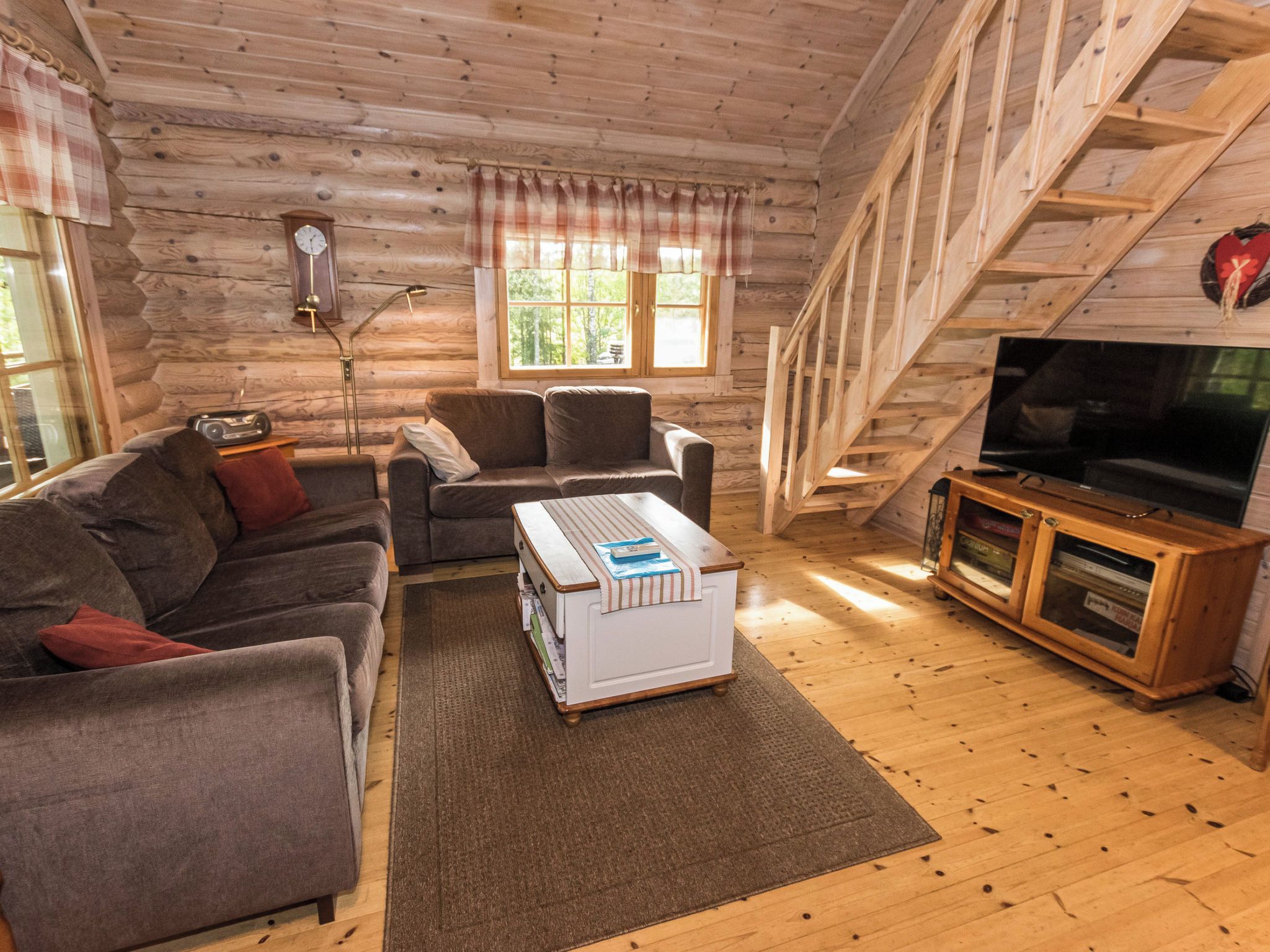 Interior acogedor de una cabaña con sofá, sillón, suelo de madera, televisor y un reloj en la pared.