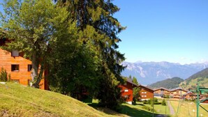 A hillside with a wooden cabin and a road leading to a mountain village. - Hyacinthe 11 by Interhome (Villars)