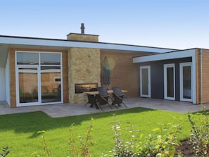 A modern house with a stone exterior, a patio with a table and chairs, and a well-maintained lawn.