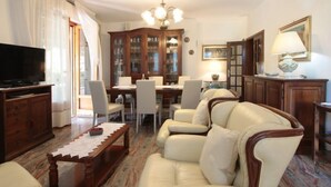 Uma sala de estar com sofá, televisão, armário de madeira e área de jantar com cadeiras e mesa.