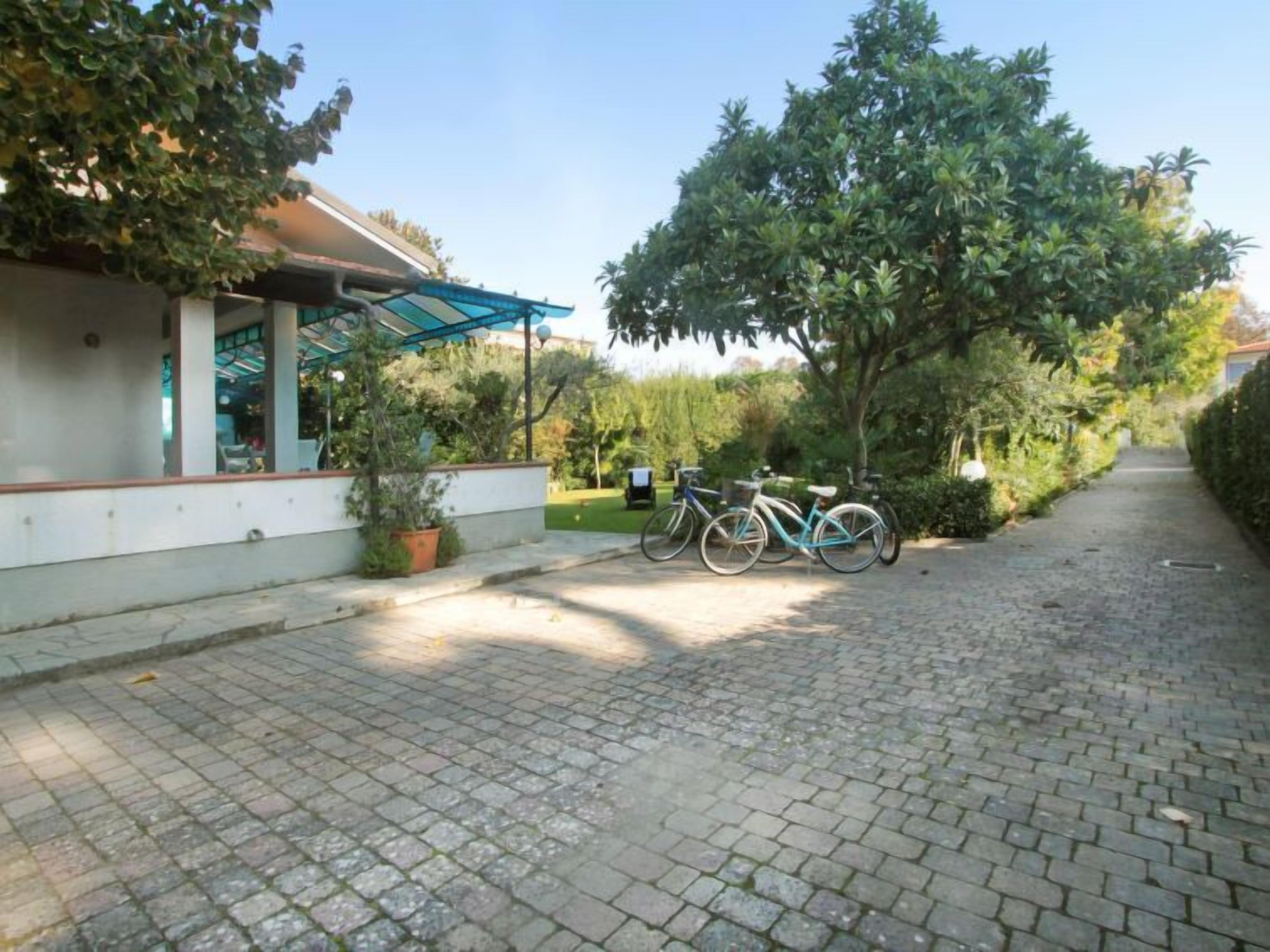 Une allée pavée mène à un bâtiment doté d’un patio couvert. Des vélos sont garés le long de l’allée.
