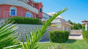 Una casa de dos pisos con fachada de piedra, color exterior rojo y un pequeño jardín con muro de piedra y follaje.