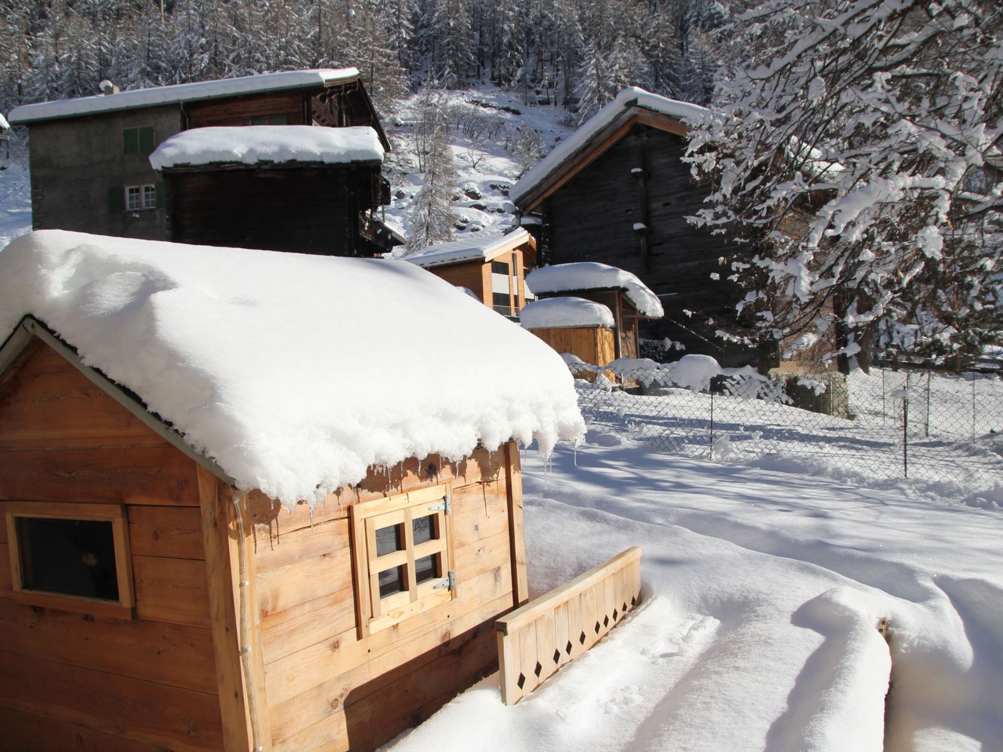 Une cabane en bois, dont le toit est recouvert de neige, entourée d’un paysage enneigé et d’arbres.