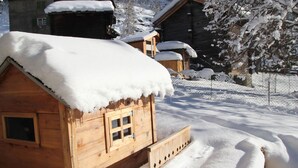 Een houten hut met een met sneeuw bedekte dak, omgeven door een besneeerd landschap en bomen.