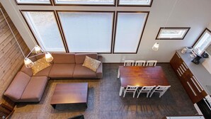 A modern interior with a sectional sofa, a dining table with chairs, and large windows offering a view of a forest.